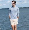 Man wearing Tradewind henley shirt and beige shorts standing by the water.