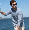 Man wearing sunglasses and a light blue long-sleeve shirt by the water