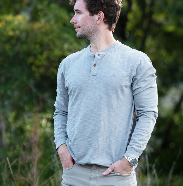 Man wearing a monument gray long-sleeve shirt standing outdoors with greenery in the background