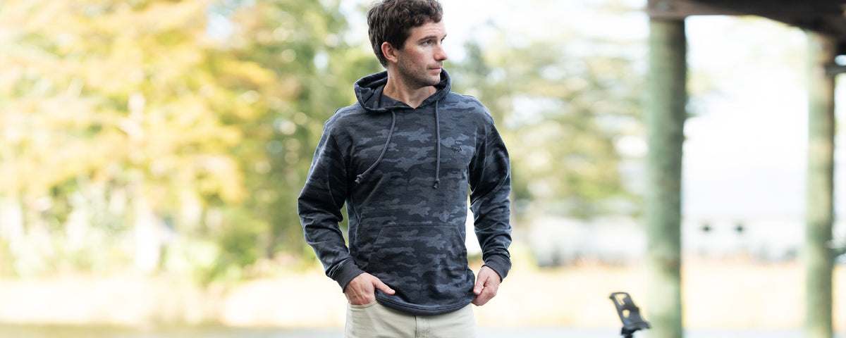 Man wearing a dark gray hoodie outdoors with trees in the background